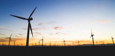 Mavi günbatımı gökyüzüne karşı kırsal tarım ortamında Eko kaynaklardan alternatif temiz yeşil güç üreten pervaneler ile yel değirmenleri İstasyonu silueti. Elektrik üreten türbinlerin çiftliği