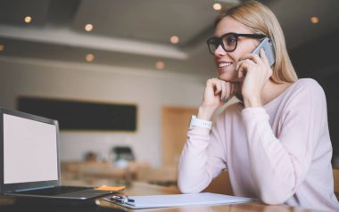 İçerik veya Web sitesi için boş ekran ile modern netbook üzerinde mesafe iş break akıllı telefon uygulaması ile arkadaş ile tebliğ göz düzeltmesi için gözlükler içinde mutlu kadın uzak işçi