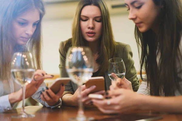 Charming female bloggers spending time togetherness for creating content text for own web pages resting with white wine in cafe interior, attractive women updating profile in social networks