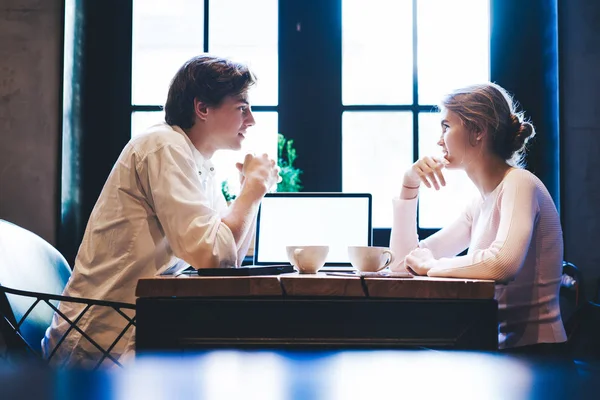 年轻的高加索男人和女人坐在自助餐桌旁 带着模拟屏幕的笔记本电脑发短信 千禧年的女生在咖啡店里谈论现代技术 — 图库照片