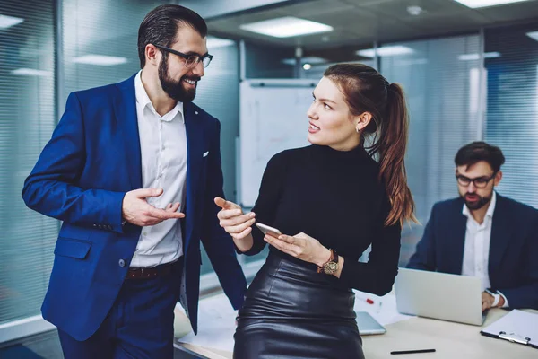 Successful business people communicating together near desktop talking about notification on modern technology, intelligent male and female entrepreneurs enjoying partnership in conference room