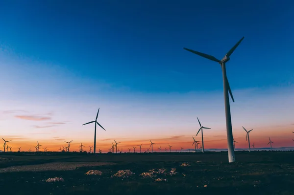 青い夕日の空に対する農村の農業環境のエコ資源から代替クリーングリーン電力を生成するプロペラを持つ風車ステーションのシルエット 電気を生産するタービンの農場 — ストック写真