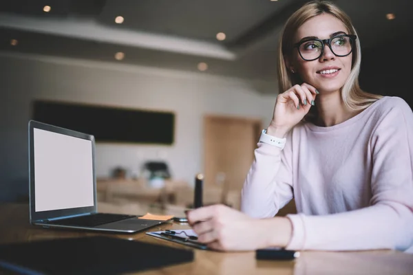 Positive hipster girl in optical spectacles thoughtful looking away in break of planning items of university course work,successful female blogger pondering on interesting ideas for publication online