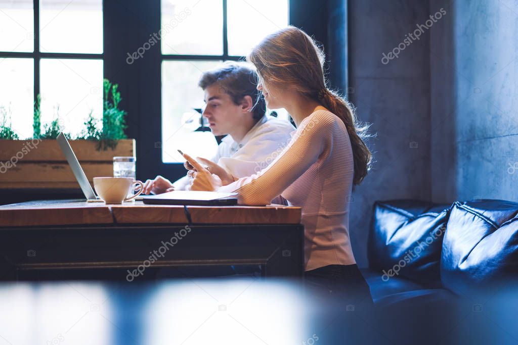 Serious millennial male and female freelancers cooperating togetherness in coworking space using good internet connection on laptop device for programming, concept of technology and communication