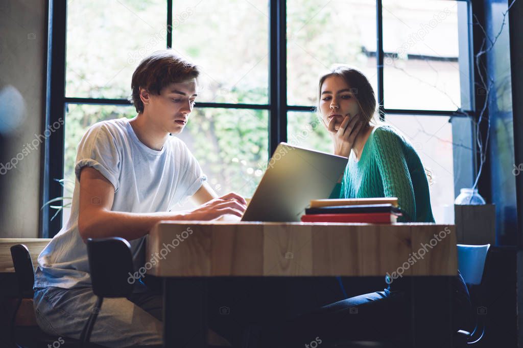 Concentrated male and female students preparing to university test for programming subject, serious man and woman reading information for creating content essay for college during collaboration
