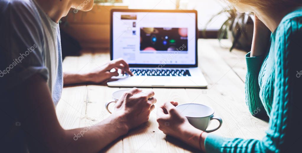 Cropped image of male and female spending time togetherness for browsing internet and chatting with friends in social network while sitting at cafeteria table with mugs, concept of relationship