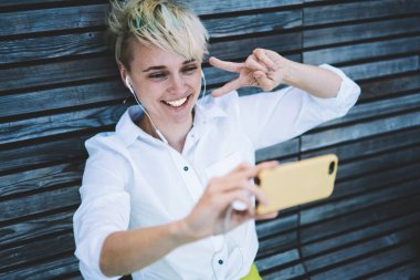 Neşeli kadın kulaklıklar ile elektronik müzik zevk ve modern hücresel komik fotoğraflar yapma, mutlu genç kadın Playlist şarkıları dinleme ve sosyal ağlarda yayın için Selfie 'ler alarak