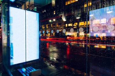 Reklam veya promosyon içeriği için boş kopya boşluk ekranı ile yağmurlu gece otobüs terminali Billboard, bilgi için lightbox kadar boş sahte, uzun pozlama ile kentsel şehir sokakta boş ekran