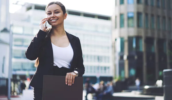 Portrait of cheerful female expert of management looking at camera during positive mobile conversation on publicity area, happy woman making good cellular call via application connected to 4g internet