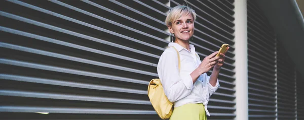 都会の設定で友人を待っている間に携帯電話を手に持つポジティブな笑顔のヒップスターの女の子 オンラインチャットのための宣伝エリアで無料Wi Fiを使用して幸せなミレニアル世代の女性ブロガー — ストック写真