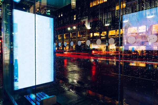 Bus station billboard in rainy night with blank copy space screen for advertising or promotional content, empty mock up Lightbox for information, blank display in urban city street with long exposure