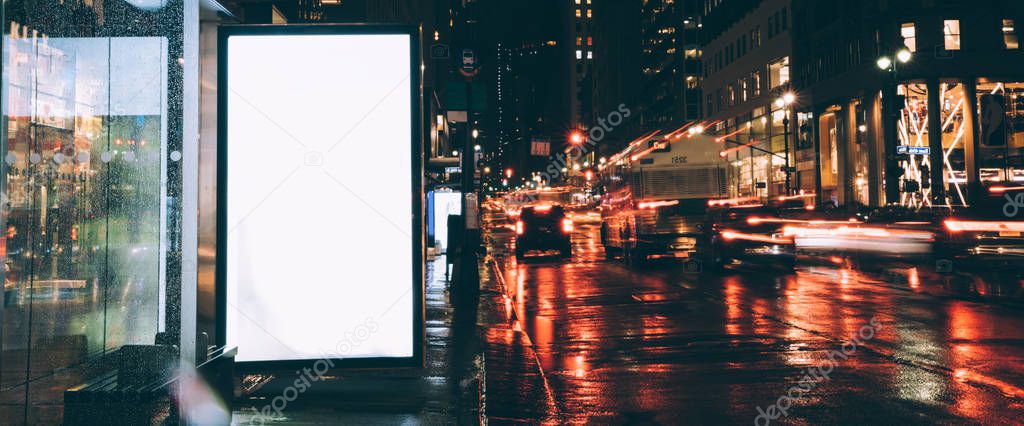 Bus station billboard in rainy night with blank copy space screen for advertising or promotional content, empty mock up Lightbox for information, blank display in urban city street with lights