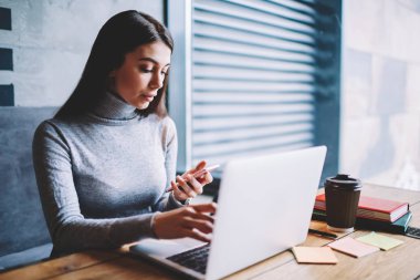 Favori kafeterya otururken ve modern dizüstü bilgisayar üzerinde çalışan meslektaşları ile sohbet için akıllı telefon kullanarak yetenekli güzel kadın grafik tasarımcı, dalgın kadın kontrol e-posta kapalı