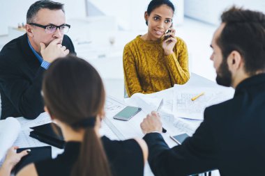 Olgun iş kadını, çok kültürlü iş arkadaşlarıyla ofis toplantısı sırasında akıllı telefon cihazıyla partneriyle iletişim kurar. Çeşitli insanlardan oluşan bir grup şirketin finans tarafını tartışır.