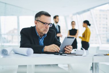 Optik gözlüklerdeki yetişkin erkek girişimci, modern dokunmatik pedde ücretsiz kablosuz internete bağlı içerik finans sitesindeki tahviller hakkında göz koruması sağlıyor.