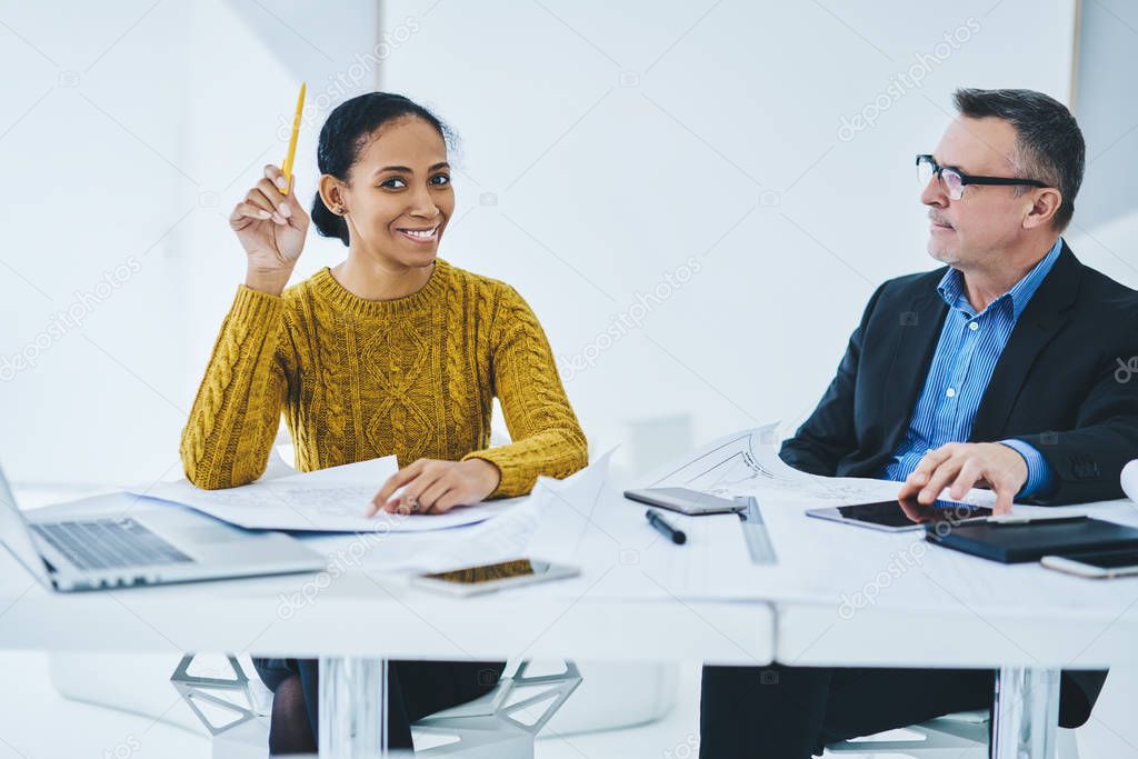 Portrait of happy successful business woman looking at camera during coworking with mature serious colleague, positive female entrepreneur analyzing management structure of company with partner