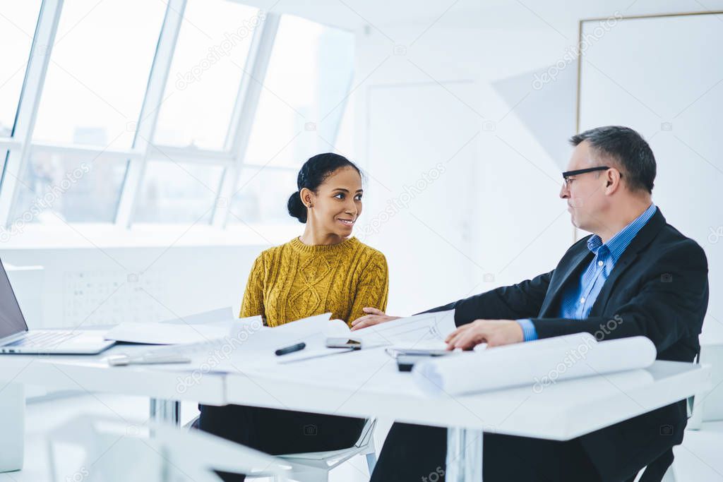 Positive male and female entrepreneurs discussing new strategy for corporate company during working time in office, successful multicultural economists talking about finance situation during meeting
