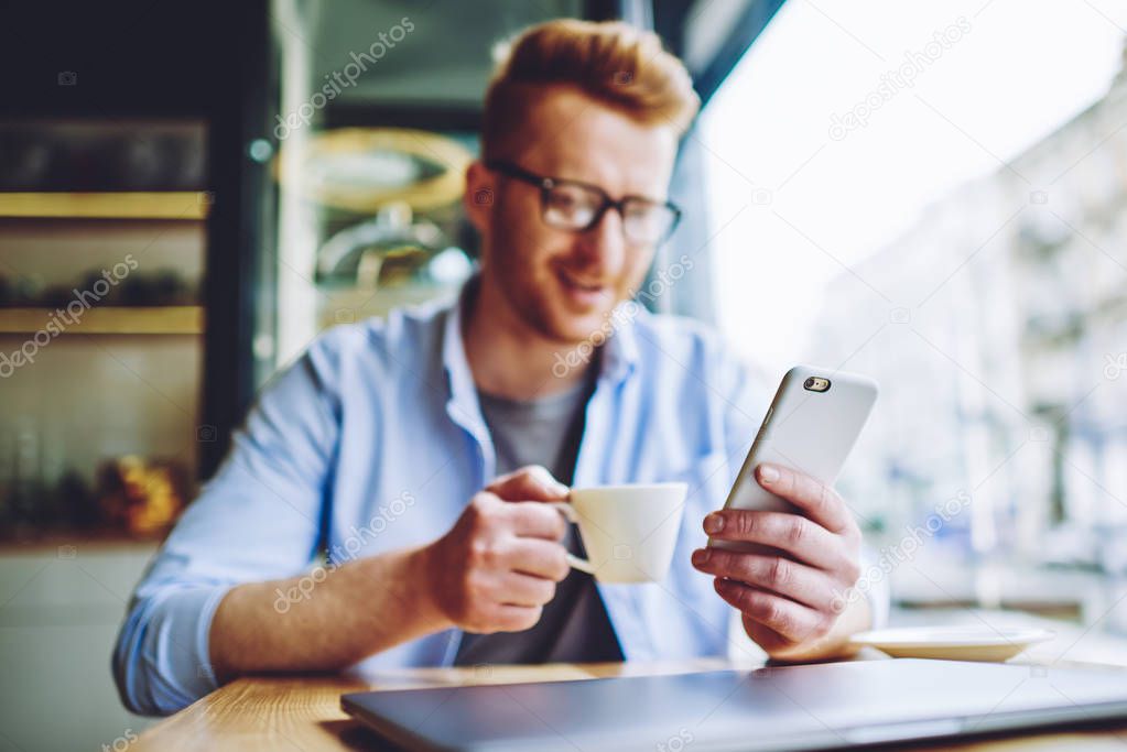 Selective focus on male hand holding smartphone device and installing new application for communicate online with friends during leisure, man watching video via cellphone during coffee time