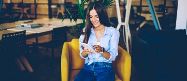 Neşeli hipster kız internet sitesinde komedi şovu izlerken dijital tablet ve ücretsiz kablosuz bağlantı kullanıyor, modern dokunmatik ped 'de internete bakıp rahat koltukta otururken gülümsüyor.