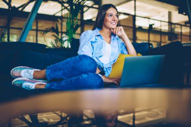 Mutlu kadın genç rahat kanepe üzerinde dinlenme ve uzak görünümlü dizüstü cihazda uygulama için bildirim yükleme için beklerken, olumlu hipster kız sohbet için boş zaman zevk