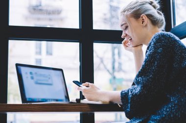 Cep telefonu ile ağ tarama yaparken akıllı telefonda komik video içeriği izlerken mutlu gülmek kadın. Kahve dükkanında otururken hücresel internette gülümseyen milenyal teknoloji Kullanıcı sörf