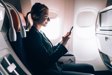 Kablosuz internet bağlantısı kullanarak cep telefonu üzerinden online sohbet gürültü iptali için Bluetooth kulaklıklar gülümseyen kadın yolcu gemide. Akıllı telefon uygulamasını kullanarak pencereden yakın koltukta genç kadın