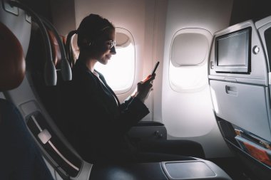 Kadın kişinin Silhouette iş gezisi sırasında cep telefonunda online video izlerken ve internet tarama için iyi bir WiFi bağlantısı gemide rahat koltuk zevk. Uygulama kullanarak uçak yolcu
