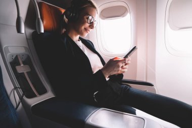 Cep telefonu arama kullanarak mutlu kadın yolcu uçak gemide WiFi bağlantısı, resmi elbise başarılı avukat hücresel uygulama üzerinden çevrimiçi sohbet müzik tadını çıkarırken