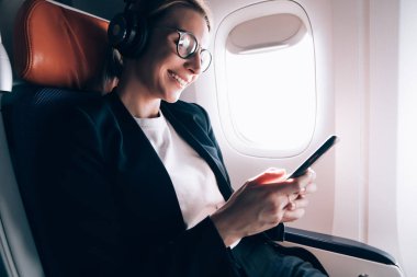 Görüntü düzeltmesi için optik gözlük neşeli kadın yolcu gemide WiFi bağlantısı kullanarak akıllı telefon uygulaması ile arkadaşlarınızla iletişimi zevk, mutlu kadın komedi film izlerken