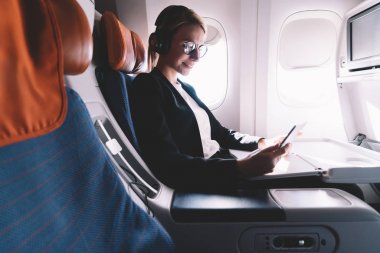 Dokunmatik yüzey ve tarama internet kullanarak gemide yüksek hızlı WiFi bağlantısı ile birinci sınıf Kıtalararası uçuş zevk gürültü iptali için kulaklıklar mutlu gülümseyen kadın yolcu