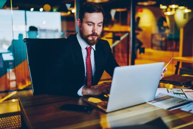 Ofis iç masada otururken modern dizüstü bilgisayar veritabanında veritabanı uygun online klavye bilgi giyinmiş sakallı gururlu CEO 'su. Netbook üzerinde Pensive işadamı online klavye e-posta