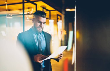 Kağıt belgesinden mali raporların bilgi okuma uygun giyinmiş Pensive sakallı başarılı girişimci. İş işadamı ofis iç ayakta muhasebe belgeleri kontrol