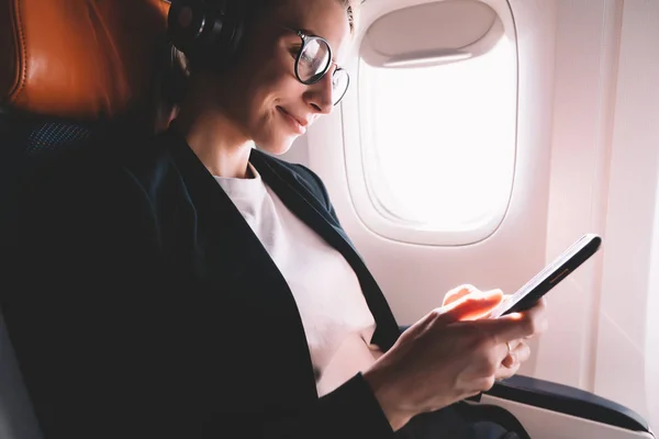 快乐微笑的嬉皮士女孩听音乐与手机在飞机上连接到无线上网机上 积极的女乘客享受头等舱飞行与良好的无线互联网在智能手机上 — 图库照片