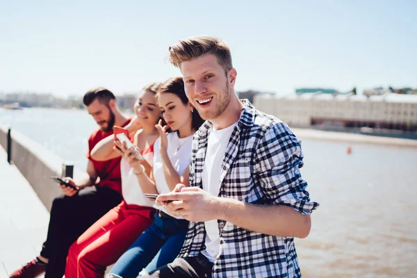 Fröhlicher Mann mit Smartphone in der Nähe von Freunden an Böschung — Stockfoto