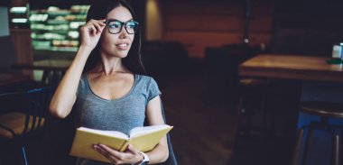 Gözlükler içinde düşünceli hipster kız bloglama hakkında profesyonel edebiyattan bilgi üzerinde durulıyor, gözlükler içinde dalgın kadın bakıyor ve en çok satan okuma için zaman hakkında düşünme