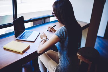 Dizüstü bilgisayar uygulama yoluyla şirket için multimedya dosyaları oluşturmak için yaratıcı kadın grafik tasarımcı çizim skeçler arka görünümü, kadın web sitesinde halk içerik makalesi için notlar yapma