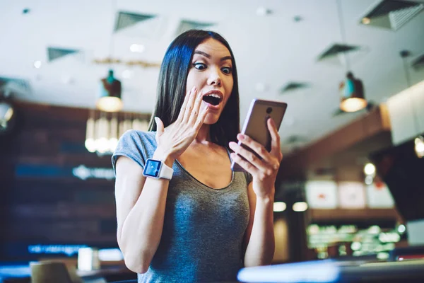 Amazed woman received email with advertising about opening new web store, surprised hipster girl communicated with colleague from work via cellular phone feeling excited about salary increase