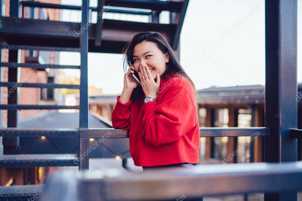 Cheerful female teenager enjoying friendly smartphone conversation for intriguer gossiping and rumors, happy chinese hipster girl making international smartphone conversation connected to roaming