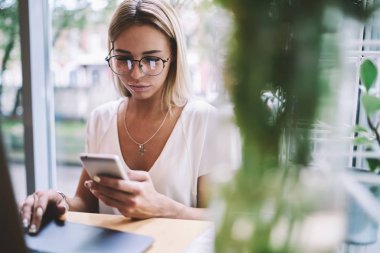 Yeni optik gözlük büyüleyici sarışın kadın bankacılık online yapmak için akıllı telefon cihazına uygulama yükleme, öğrenme için bilgi aramak için teknolojileri kullanarak genç kadın öğrenci