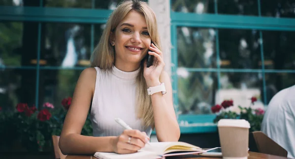 Freelancer sonriente hablando en smartphone y escribiendo en notebook —  Fotos de Stock