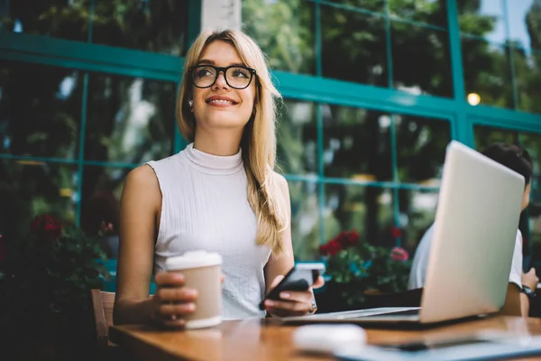 Freelancer con bebida caliente y smartphone mirando hacia otro lado —  Fotos de Stock