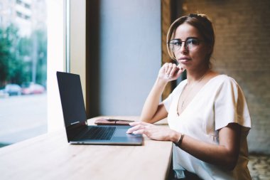 Uzaktan çalışan çekici kadın programcı portresi ve yeni Web sitesi oluşturma break kamera bakıyor, yeni modern Netbook ile masada oturan optik gözlük güzel yetenekli kadın