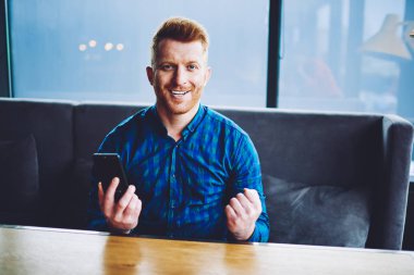 Sosyal ağlarda kendi web sayfası hakkında istatistiklerden heyecanlı mutlu duygusal erkek blogger duygu Portresi, elinde modern akıllı telefon gadget ile müreffeh hipster adam kameraya bakarak