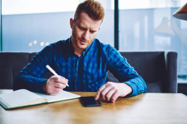 Eğitim için ders kitabı ile sınava hazırlanırken yeni modern cep telefonu 4g internete bağlı üniversite web sitesinde üniversite programı hakkında konsantre erkek öğrenci okuma haberleri