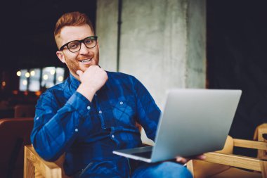 Şık gözlük neşeli erkek freelancer portresi coworking alanında dizüstü bilgisayar ile otururken kameraya bakarak, netbook ile uzaktan çalışma için zaman zevk mutlu gülümseyen adam