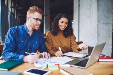 Başarılı grafik tasarımcıları işbirliği alanında işbirliği sırasında şirket için yeni logo oluşturma, pozitif çok kültürlü erkek ve kadın hipsters dizüstü bilgisayar cihazı üzerinde işbirliği için zaman zevk