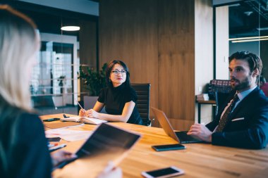 Modern ofis içinde çalışan çeşitli erkek ve kadın ortaklar dizüstü bilgisayarla toplantı masasında işbirliği yapıyorlar. Çok kültürlü meslektaşlar finansal stratejiyi tartışıyorlar.