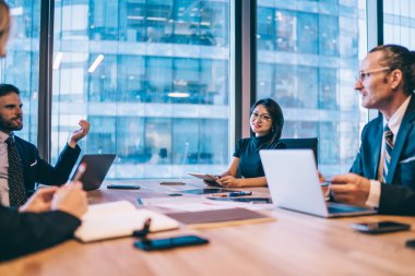 Resmi giyinmiş başarılı erkek ve bayan meslektaşlar modern ofis odasında iş birliğinin keyfini çıkarıyor masaüstünde oturuyor ve veri bilgilerini, finansal beyin fırtınası kavramını tartışıyorlar.