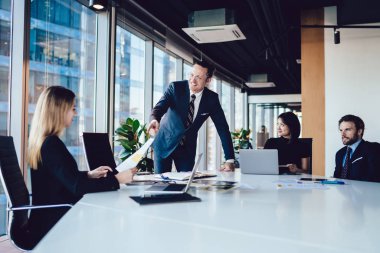 Resmi giyinmiş başarılı erkek patron, mali rapordan veri kontrolü için yapılan beyin fırtınası toplantısında çalışanlarla iletişim kurarken, ofis içi iş birliği yaparken,