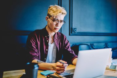 Çinli bir adam bilgisayar aygıtında program kodu oluşturmak için serbest çalışan yeni bir uygulama yüklüyor. Hippi adam internet bağlantısı kullanarak internet üzerinden webinar izliyor.